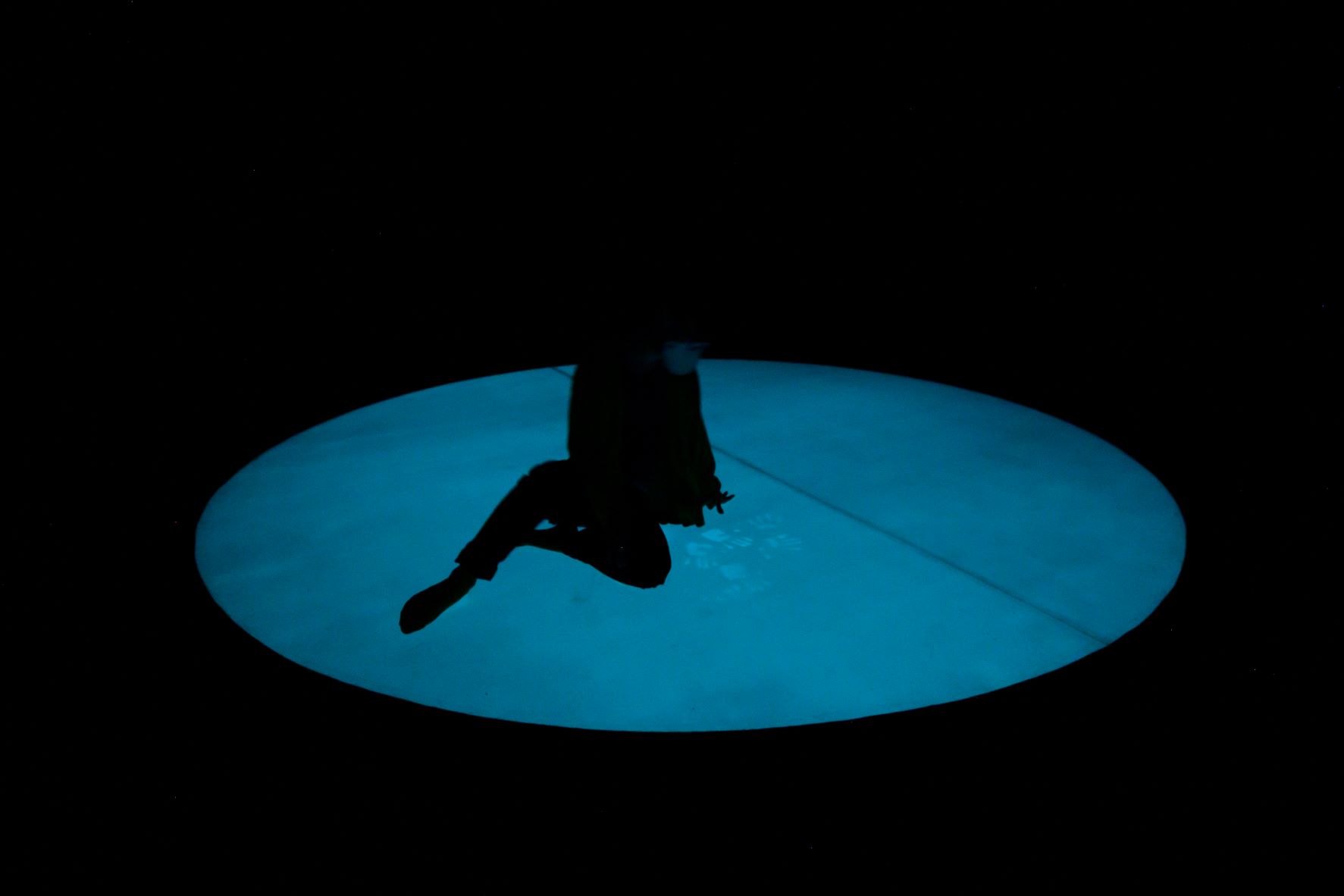 A person sits on a glowing blue circle. In front of them are handprints on the blue surface.