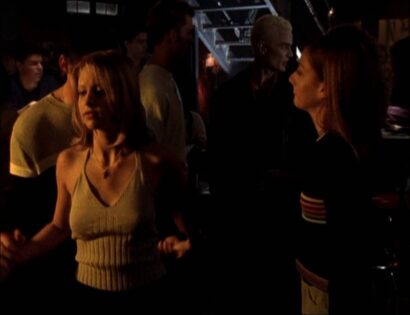 A photo of Sarah Michelle Geller as Buffy dancing in a dimly lit club. She is a blonde, white woman and she wears a knit green tank top.