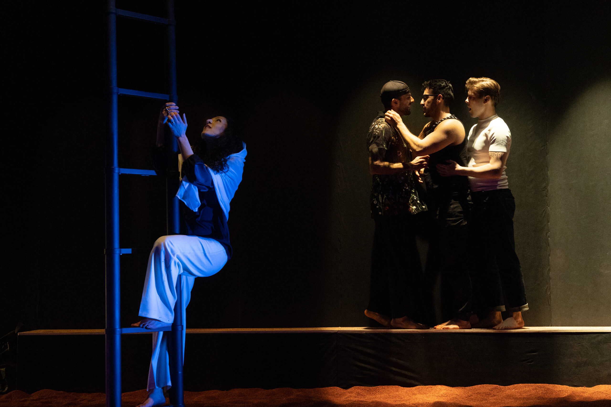 A woman climbs a ladder on the left side of the image. On the right, three men embrace in a dimly lit scene.