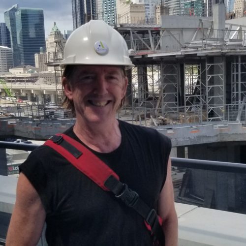 Paul Therrien outside wearing a construction safety hat and smiling in front of a construction site