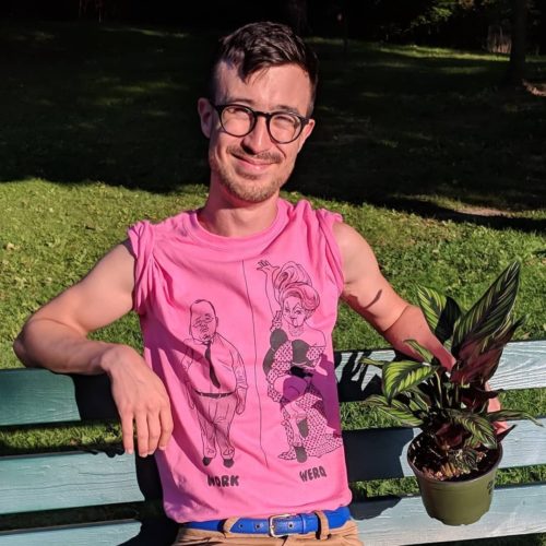 Aidan sitting outside on a bench wearing a pink shirt and holding a plant