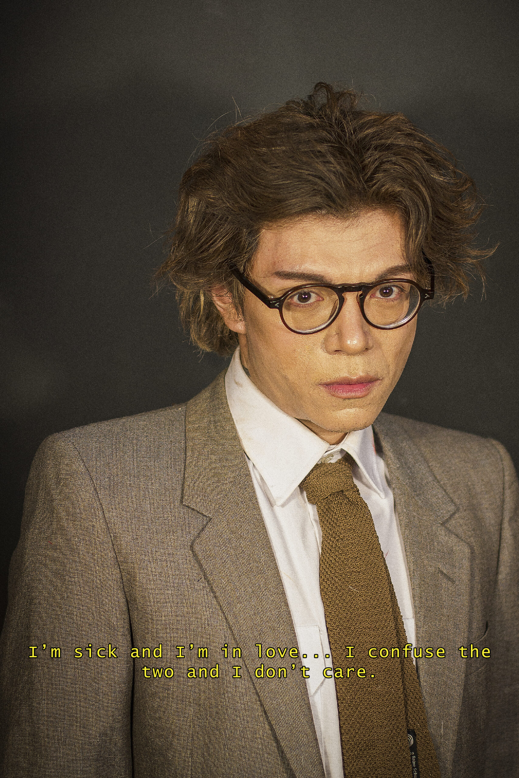 Jaime has messy brown hair and glasses. He wears a white shirt, brown knit tie and a brown blazer. At the bottom of the image, text reads "I'm sick and I'm in love... I confuse the two and I don't care."