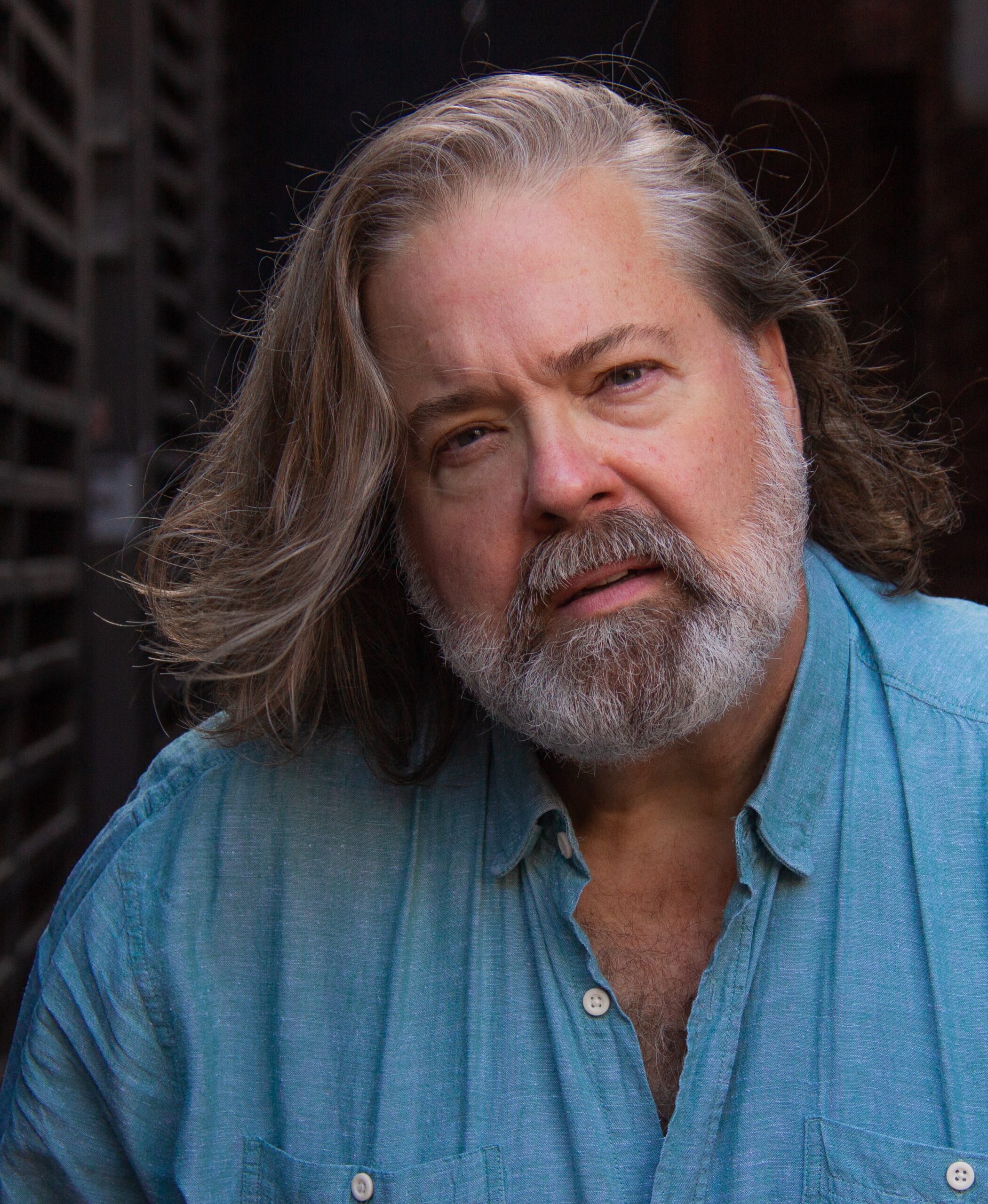 Headshot image of Bruce Dow. Bruce is wearing a blue collared shirt and has shoulder length grey hair and a grey beard.