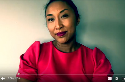 Video clip screenshot of Catherine Hernandez wearing red lipstick and a red blouse