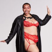 Image of drag performer in red lingerie and a long black coat, striking a pose.