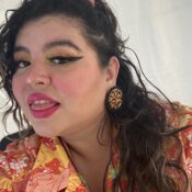 Image of Pansy Chisk, wearing eye liner and red lipstick, and a red and orange floral shirt.