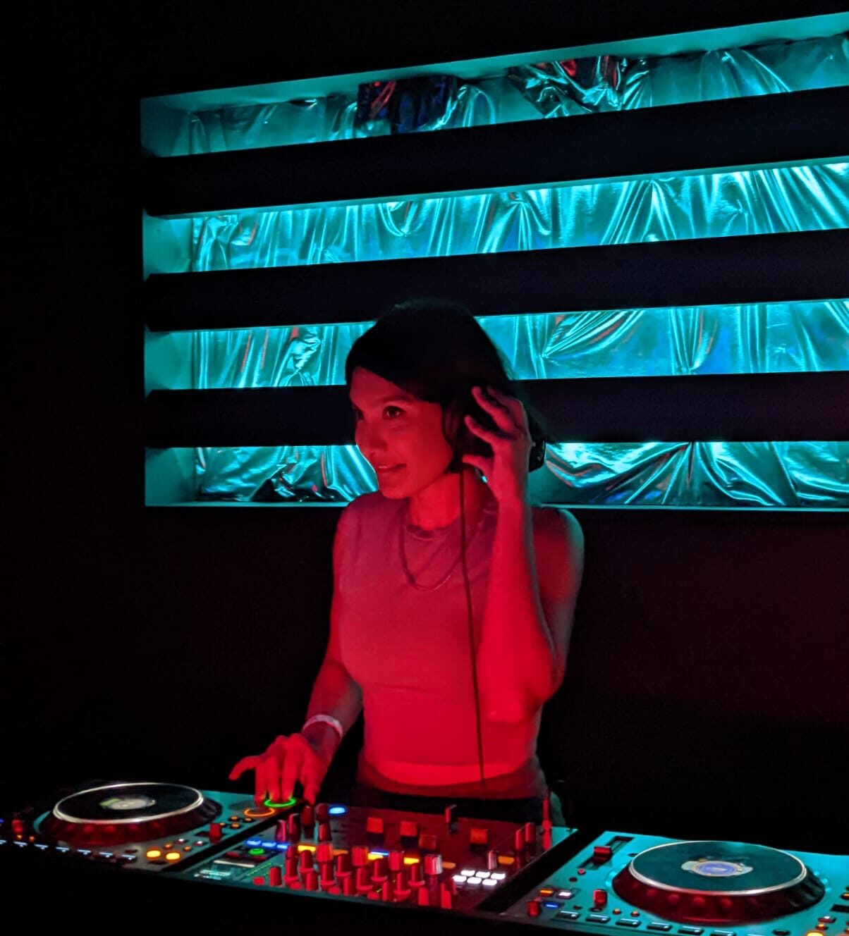 Image of Marium DJing, with blue and silver lighting behind her.