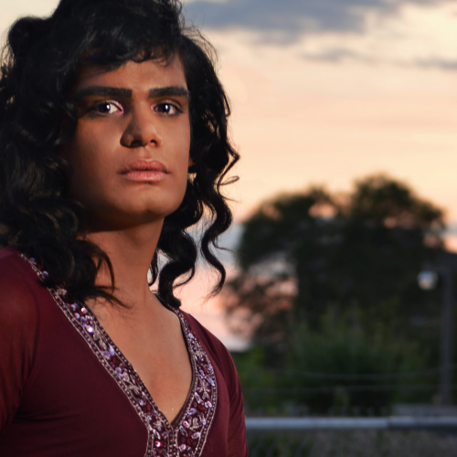 Headshot image of Bilal Baig. Bilal is wearing a read deep v top and has curly dark hair just passed their shoulders.