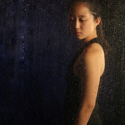 Asian woman standing beside window with rain