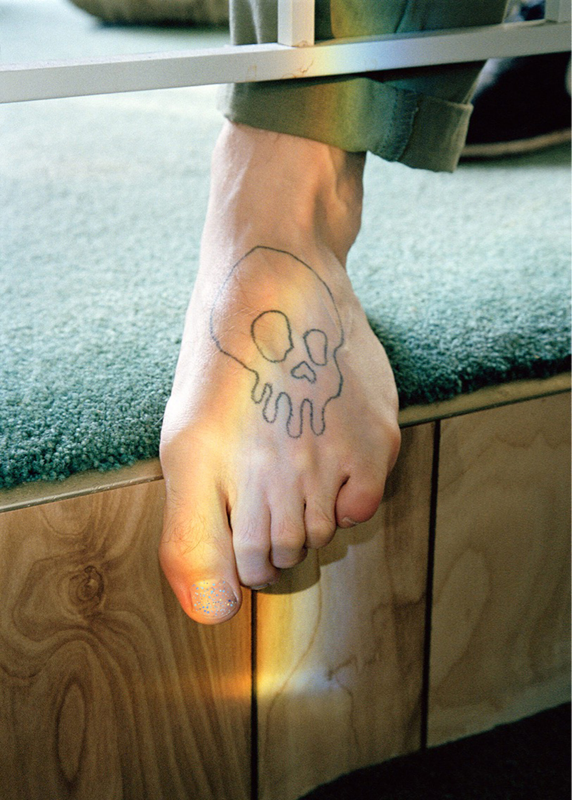 Image of a foot with a skull tattoo and glittery toenail polish.