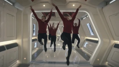 An image of five actors in Star Trek Uniforms- red long sleeve shirts and black pants. They are jumping in the hall of a space ship that looks very white, shiny and sterile.